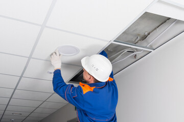 foreman in blue uniform and white hard hat, installed a lighting lamp in the false ceiling