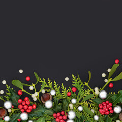 Decorative Christmas background border with silver baubles, winter greenery of fir holly, cedar...