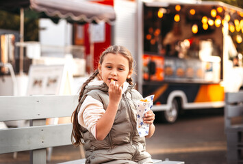 Little girl eating rench fries with sauce at street cafe outside. Concept of fast food and children.