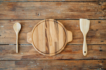 High-quality kitchen utensils. A round textured plate of light wood is located on the table,a spoon and kitchen spatula lying nearby, the frame is on top. Set for a kitchen.