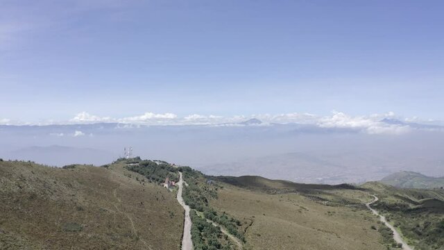 Drone shot over the moorlands of the Andes in Rucu Pichincha near Quito, Ecuador. A trail surrounded by trees is seen as well as a church on the side. Mountains are seen on the back.
