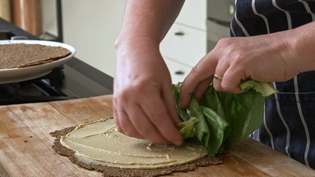 Chef tucks lettuce inside flaxseed wrap with hummus spread