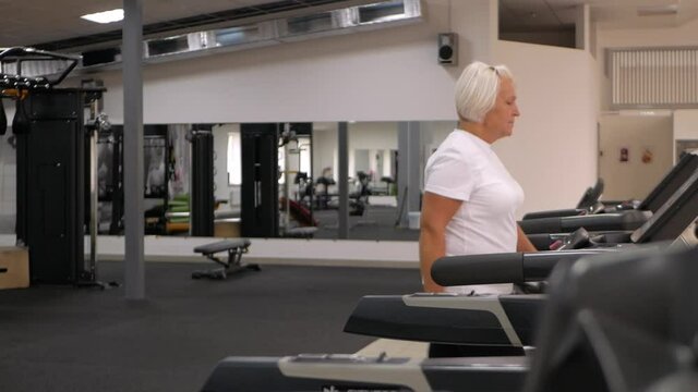elderly woman with gray hair plays sports in gym. Active healthy lifestyle, pensioner, senior concept. Rehabilitation after injuries, strengthening immunity, losing weight, racecourse.