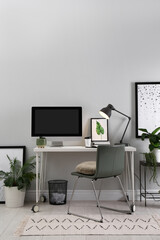 Comfortable workplace with modern computer and houseplants in room. Interior design
