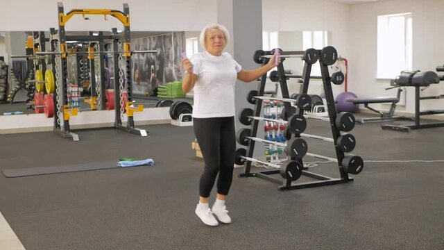 elderly woman with gray hair plays sports in gym. Active healthy lifestyle, pensioner, senior concept. Rehabilitation after injuries, strengthening immunity, losing weight, well-being. jumps rope
