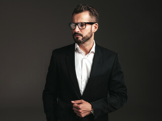 Portrait of handsome confident stylish hipster lambersexual model. Sexy modern man dressed in elegant black suit. Fashion male posing in studio on dark background. In spectacles