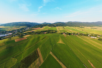 Aerial view of agricultural green fields and residential building in small european town near mountains. Nature landscape