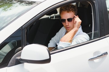 Naklejka premium Electric car driver - green energy biofuel concept. Male behind wheel. Man driving new ecofriendly vehicle Young male owner proud confident looking at camera, Taxi driver concept.