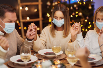 Friends praying before christmas dinner wearing mask.