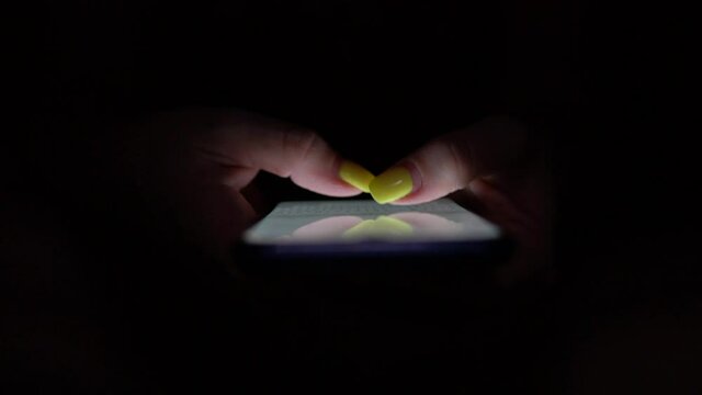 Doomscrolling. Young female checking on her phone during the night. Bright touchscreen scrolling in the dark. Browsing social networks. Procrastination before sleep. Girl using smartphone.