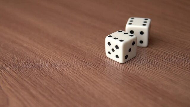 Throwing two white plastic gaming dices on a wooden surface. Rolling playing cubes. Gambling risk and luck, game chances for win and losing, probability theory. 