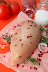 Raw chicken fillet with ingredients on orange background