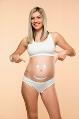 Fototapeta premium Future mother showing a smiley face drawing on belly on a beige background