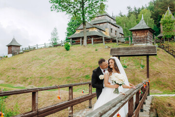 Newlyweds stand on a wooden bridge on the background of the church.