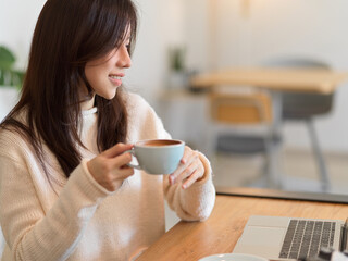 Beautiful woman drinking morning coffee while working on laptop computer at cafe bar.