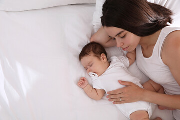 Young mother resting near her sleeping baby on bed, top view. Space for text