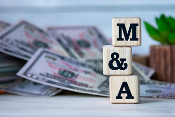 M and A - acronym on wooden cubes on the background of a cactus and banknotes