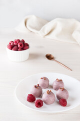 Raspberry truffles in pink chocolate on a white plate. Sugar, gluten and lactose free.