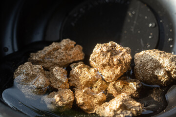 Profit, trade and exchange. Gold nuggets spilling out from a grungy old metal container, placed on a old wooden table.Shallow depth of field.selective focus.