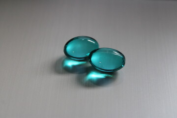 Two blue liquid gel capsules on silver-colored surface