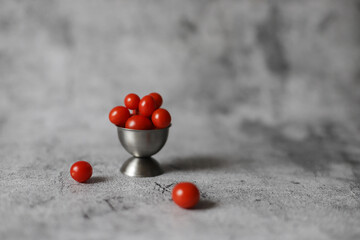 Small red candy tomatoes in steel plate on grey background.
