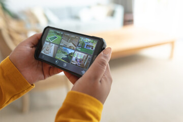 Hands of african american plus size woman checking view from security cameras on smartphone