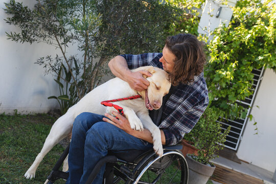 Caucasian disabled man sitting on wheelchair playing with his dog in the garden