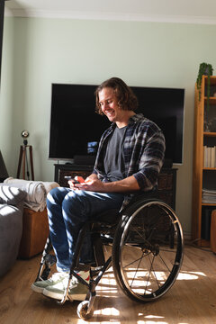 Caucasian disabled man sitting on wheelchair smiling while using smartphone at home