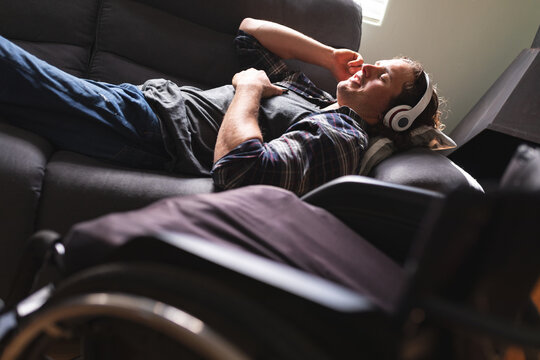 Caucasian disabled man wearing headphones listening to music while lying on the couch at home