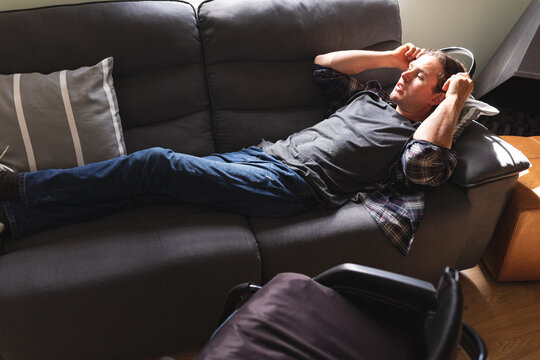 Caucasian disabled man wearing headphones while lying on the couch at home