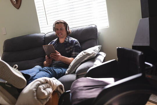 Caucasian disabled man wearing headphones using digital tablet sitting on the couch at home