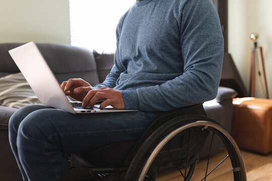 Mid section of disabled man sitting on wheelchair using laptop at home