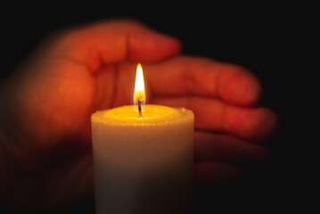 One palm take care of candle fire at night.Selective focus,Dark black background.Closeup.