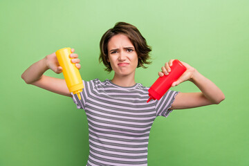 Photo of sad young brunette lady hold ketchup mustard unhealthy food wear striped t-shirt isolated on green color background