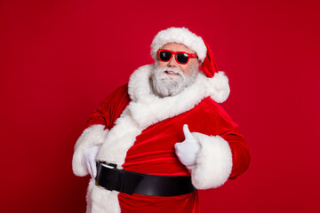Portrait of attractive cheerful Santa showing thumbup advert ad recommend isolated over bright red color background