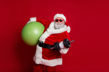 Photo of handsome strong santa claus wear red costume hat dark holding fitball building muscles isolated red color background