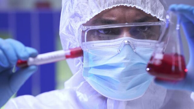 Indian scientist in medical mask holding flask and test tube with blood sample