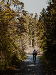 Fototapeta premium Woman cyclist riding along a road in autumn forest. Road cycling in forest.