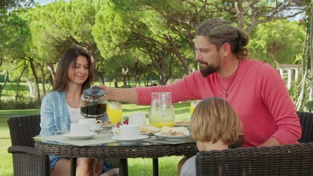 Happy family time have a breakfast outdoor, with picturesque nature around. Lovely parents and a kid enjoy their summer vacation at luxury hotel terrace. High quality 4k footage