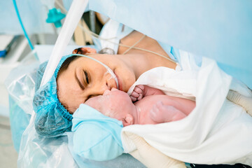 The first moments of mother and newborn after childbirth. Newborn child seconds and minutes after birth. Premature baby boy delivered by Caesarean section, being shown to his mother. - Powered by Adobe