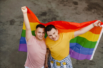 Young gay couple standing with rainbow flag during pride parade