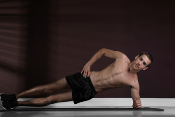 Fototapeta na wymiar Handsome man doing side plank exercise on floor indoors