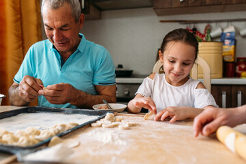 family traditions, grandfather and granddaughter make dumplings together at the table, grandfather helps granddaughter