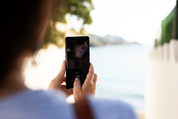Young woman taking photo with phone near the sea. Happy woman enjoy in sunny day.