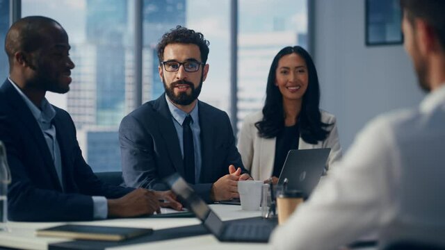 Modern Multi-Ethnic Office Conference Room Meeting: Diverse Team of Top Managers Talk, Brainstorm, Use Computers. Businessman Presenting Investment Strategy to Partners. Slow Motion Medium Close-up