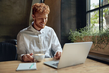 Young man drinking coffee near laptop in cafe