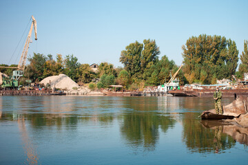 older man is fishing on the river. Dirty water, pollution, garbage, rusty barges. Ecological catastrophe, production waste. sunken boats