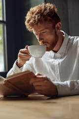 Young redhead man reading book in cafe