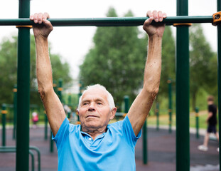 Obraz premium mature cheerful pensioner man doing physical exercises on sports equipped playground