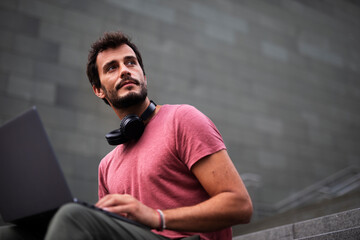 Handsome man working with laptop on city street. Man using his laptop while sitting on stairs outdoors.